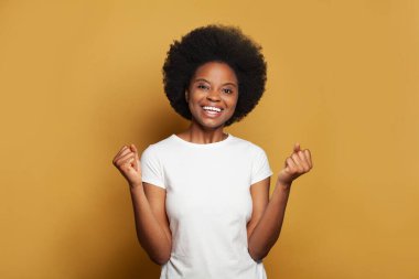 Beyaz tişörtlü hoş genç bir kadın. Parlak sarı stüdyo duvarına gülüyor ve eğleniyor.