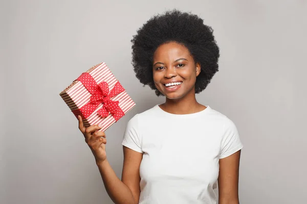 stock image Beautiful smiling woman wearing white t-shirt showing red gift box against white studio wall banner background