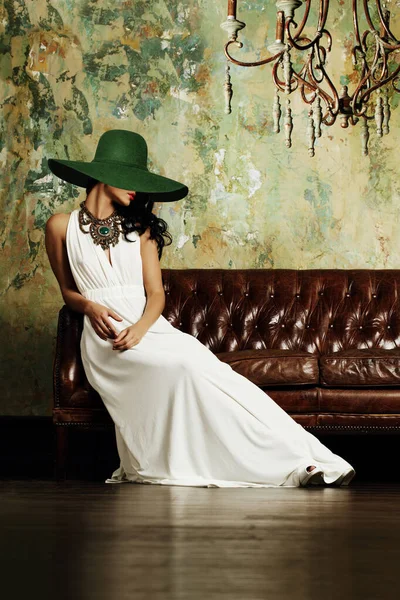 Κομψό Μελαχρινή Γυναίκα Ποζάρουν Πράσινο Ευρύ Brim Καπέλο Στον Καναπέ — Φωτογραφία Αρχείου