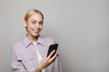 Beyaz stüdyo arka planında akıllı telefon kullanan mutlu bir kadın.