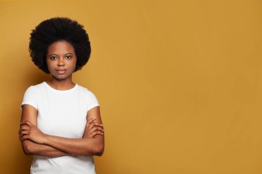 Beyaz tişörtlü, sarı stüdyo arka planında kendine güvenen siyah bir kadın.