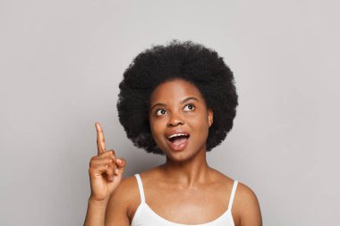 Happy young woman pointing up her finger on white studio wall background. Beautiful female model with fresh clean skin