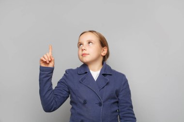 Clever child girl in school uniform pointing and looking up against grey studio wall background