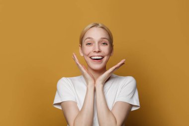 Portrait of happy attractive woman laughing and looking at camera against yellow studio wall background.