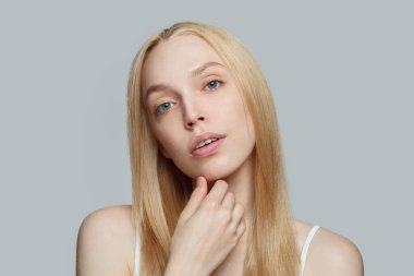 Glamorous woman with long blonde hair isolated on grey background. Beauty, cosmetics, skincare, glamour