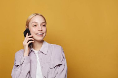 Portrait of a happy young woman using mobile phone on yellow studio wall background