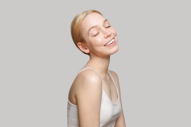 Fresh blonde woman in white top smiling isolated on grey background. Beauty, cosmetics, skincare, glamour