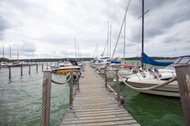 Yachts and boats on wooden pier, cloudy sky