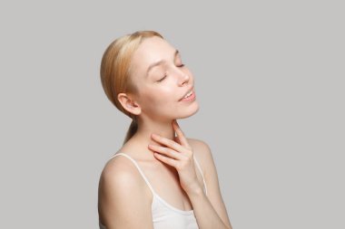 Fresh blonde woman standing sideways isolated on grey background. Beauty, cosmetics, skincare, glamour