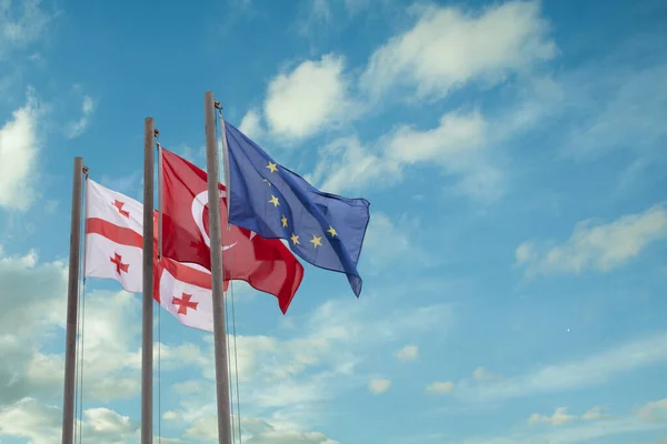 Georgian, Turkish and Europen Union flags on the background of blue cloudy sky