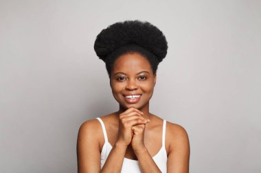Beyaz stüdyo duvarının arka planında gülümseyen, temiz, taze, koyu tenli, güzel, genç, esmer bir kadın. Cilt bakımı ve yüz tedavisi kavramı