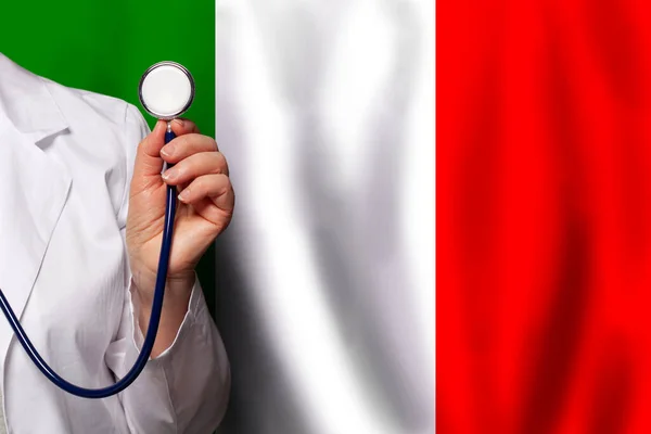 Italian doctor\'s hand with stethoscope on the background of flag of Italy Medicine, clinic, practitioner, healthcare