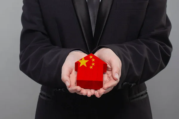Chinese person holding wooden house with flag of China Finance, investment, mortgage, loan and credit concept