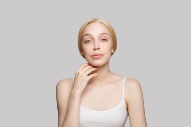 Gri arkaplanda yüzüne dokunan sevimli bir kadın. Güzellik, kozmetik, cilt bakımı, cazibe.