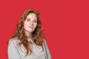 Kırmızı stüdyo arka planında gri kazaklı, dalgın esmer kadın.