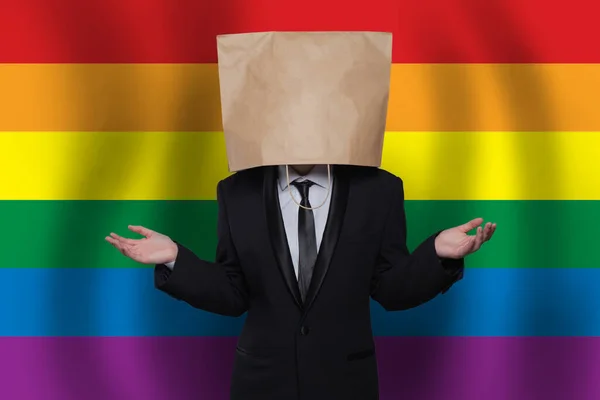 Businessman with paper bag on head on the background of LGBT flag. Equality, diversity, freedom concept