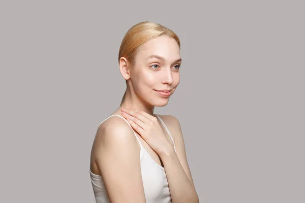 Woman with blonde ponytail standing sideways isolated on grey background. Beauty, cosmetics, skincare, glamour.