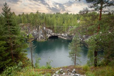 Bulutlu gökyüzü, yeşil ağaçlar ve dağ gölü