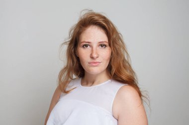 Kızıl saçlı, makyajlı, beyaz arka planda kameraya bakan mükemmel bir kadın model.