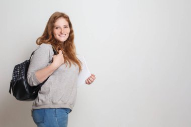 Beyaz stüdyo duvarına karşı duran mutlu öğrenci kadın.