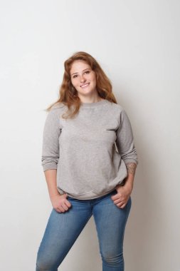 Beyaz duvar arkasında duran neşeli model kadın, stüdyo portresi.