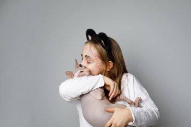 Beyaz stüdyo arka planında kedi yavrusuna sarılan kedi yüzlü çocuk.