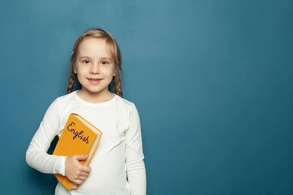 青の黒板の背景に英語の本を持つ子供の学生の女の子 — ストック写真