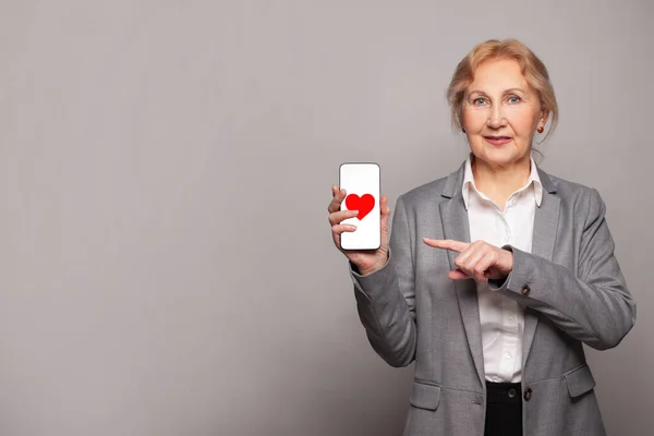 幸せな成熟したビジネス女性表示上の赤いハートと現代的なスマートフォンを示す — ストック写真