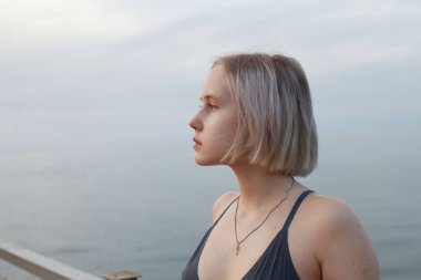 Deniz ve bulutlu gökyüzünün arka planında duran kolsuz tişörtlü kadın portresi