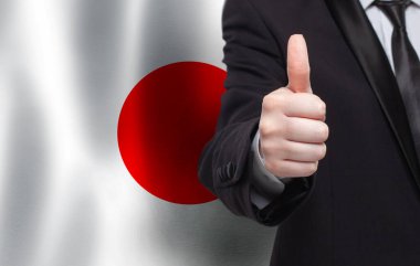 Japon konsepti. Japon bayrağının arka planında baş parmağını gösteren bir iş adamı