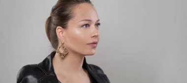 Güzel esmer kadının kulağında altın bir küpe Gri pankartta yakın plan