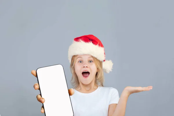 Feliz Menina Surpresa Santa Mostrando Smartphone Com Tela Branca Vazia — Fotografia de Stock