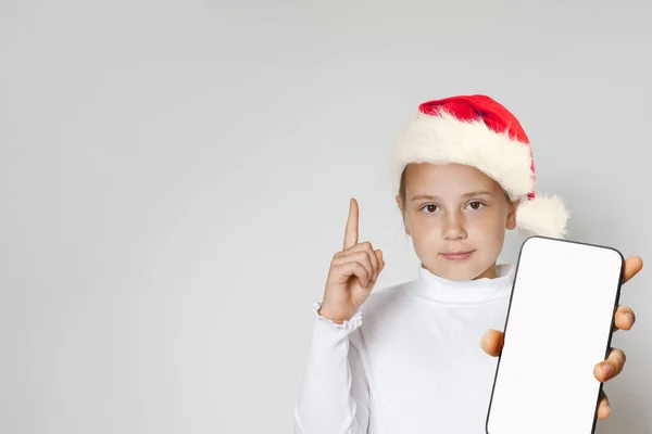 幸せな愛らしい子供の少女サンタは スマートフォンが灰色の背景を指摘しています クリスマスの肖像画 — ストック写真