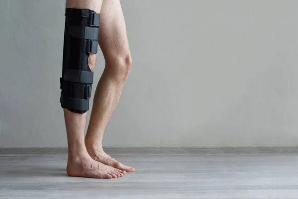 Knee brace on male leg on gray background. Injury, arthritis and meniscus diseases concept.