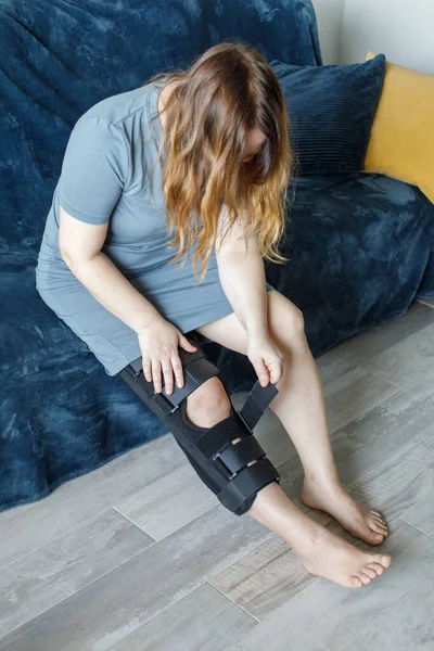 Woman wearing knee brace at home. Orthopedic Anatomic Orthosis. Braces for knee fixation, injuries and pain