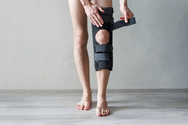 Male leg wearing knee brace on gray background. Orthopedic Anatomic Orthosis. Braces for knee fixation, injuries and pain. Foot orthosis tutor