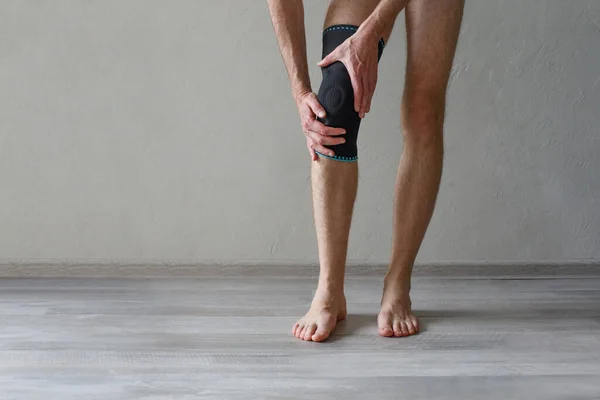 Knee Support Brace on male leg on grey background. Elastic orthopedic orthosis. Anatomic braces for knee fixation, injuries and pain. Protective knee joint bandage sleeve. Trauma, rehabilitation concept.