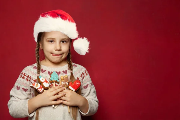 クリスマス ガールズ 子供は赤い背景にジンジャーブレッドクッキースノーマン サンタクロースのトナカイとXmasツリーを保持しています — ストック写真