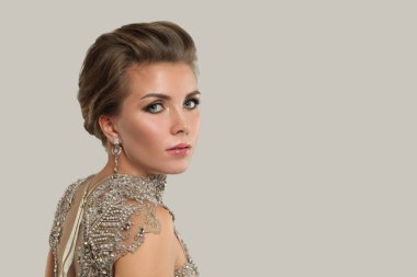 Taze parlak ciltli, sağlıklı saçlı ve makyajlı güzel bir kadın gri afiş arkaplanındaki kameraya bakıyor.