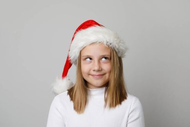 Noel Baba şapkalı şirin yaramaz kız beyaz arka plana bakıyor.