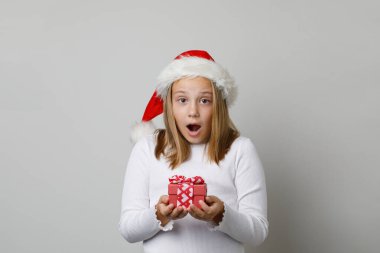 Noel ve Yeni Yıl konsepti. Mutlu, heyecanlı, şok olmuş, beyaz arka planda ağzı açık, Noel Baba şapkalı kız çocuğu.