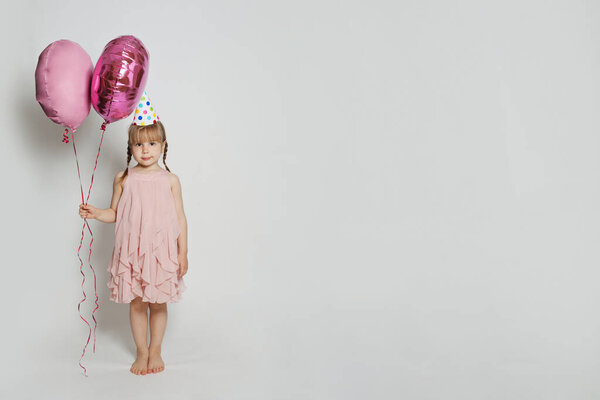 Cheerful child holding two pink balloon on white studio wall banner background. Happy birthday background card