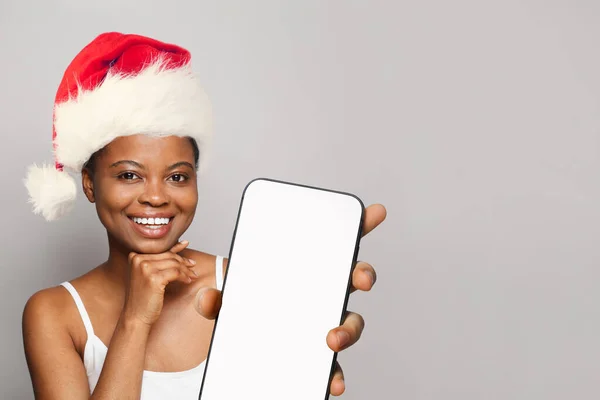 スマートフォンを示すサンタの帽子をかぶっている幸せな笑顔の女性 — ストック写真