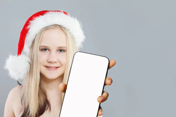 空白の白いスクリーンの表示が付いているスマートフォンを示すかわいい子供のサンタのクリスマスの写真 適用かウェブのためのモックアップの旗 — ストック写真