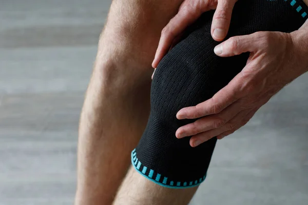 Knee Support Brace on male leg on grey background. Elastic Orthopedic Anatomic Braces for knee fixation, injuries and pain. Knee Joint Bandage Sleeve