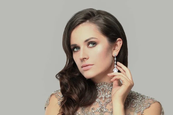Pretty glamorous brunette model woman with makeup and wavy hairstyle wearing luxurious diamond earring and shiny dress