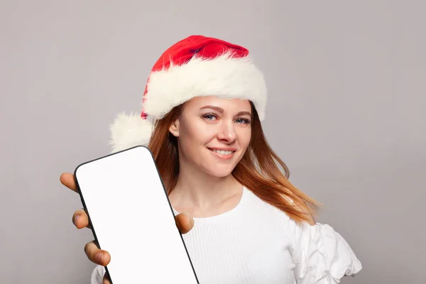 スマートフォンディスプレイを表示する赤いサンタの帽子で完璧な女性のクリスマスの肖像画 — ストック写真