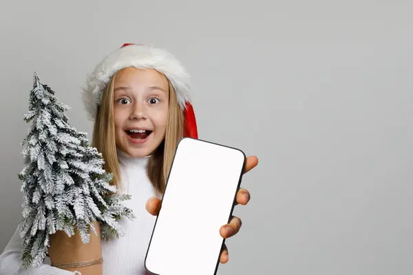 空白の白いスクリーンの表示 クリスマスの概念が付いているスマートフォンを握っている幸せな興奮した子供の少女 — ストック写真