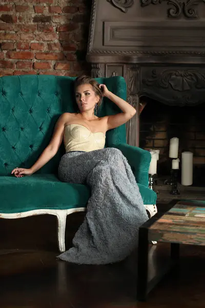 穿着晚礼服的优雅漂亮迷人的女时尚模特坐在豪华室内装饰的绿色沙发上 — 图库照片