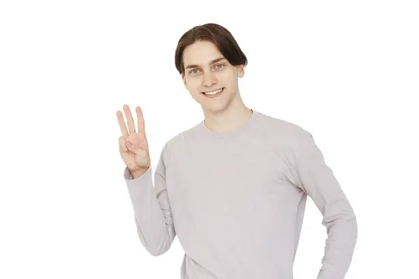 照片上 一个快乐的年轻人微笑着看着摄像机 用三只手指头在白色的背景上看 — 图库照片